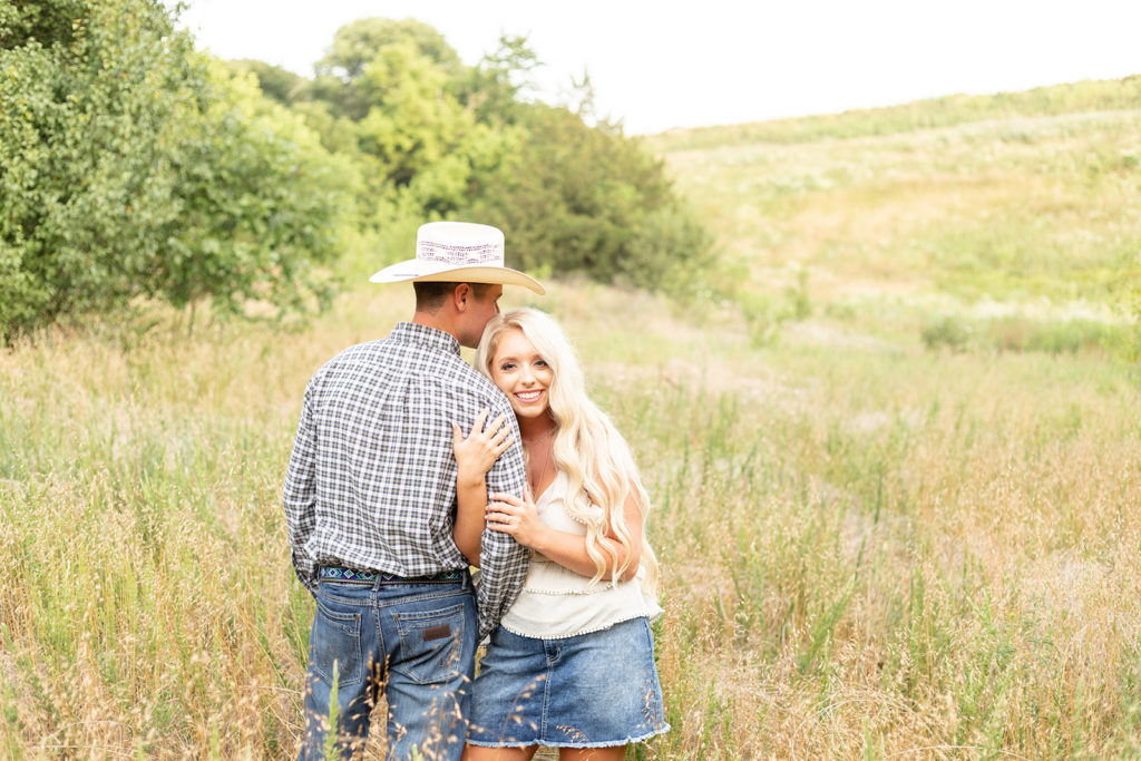 Man in cowboy hat, and woman standing in open field during engagement photography session