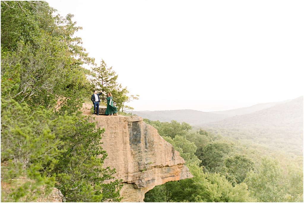 couple standing along a rock cliff face, dancing during Engagement Photography session in NWA