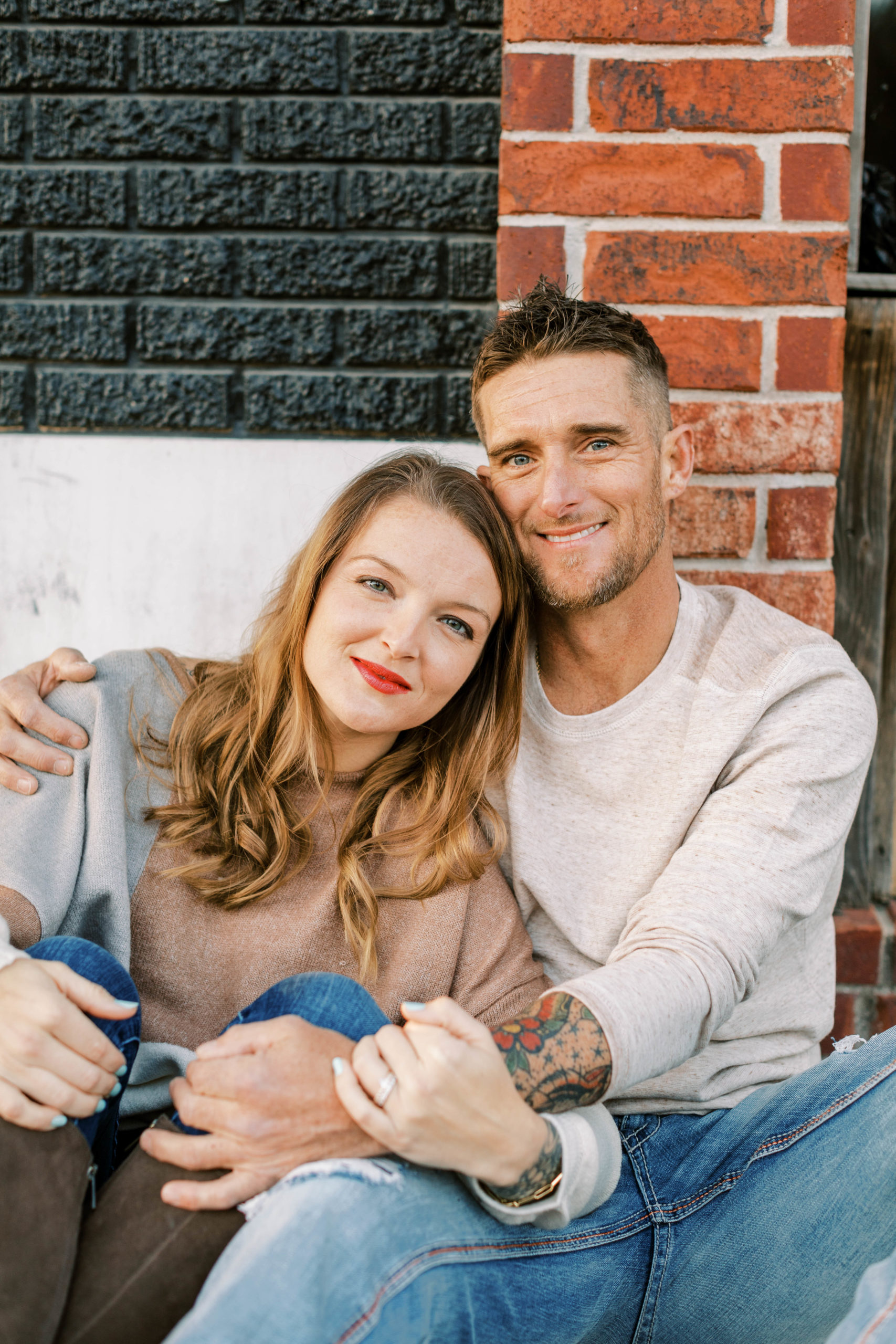 Man and Woman sitting in front of brick wall during engagement photography session
