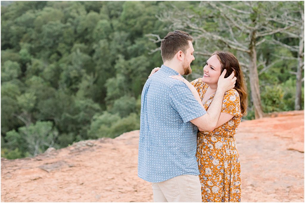 Man and Woman standing on a cliff, his hands running through her hair - picture taken by Engagement Photographer
