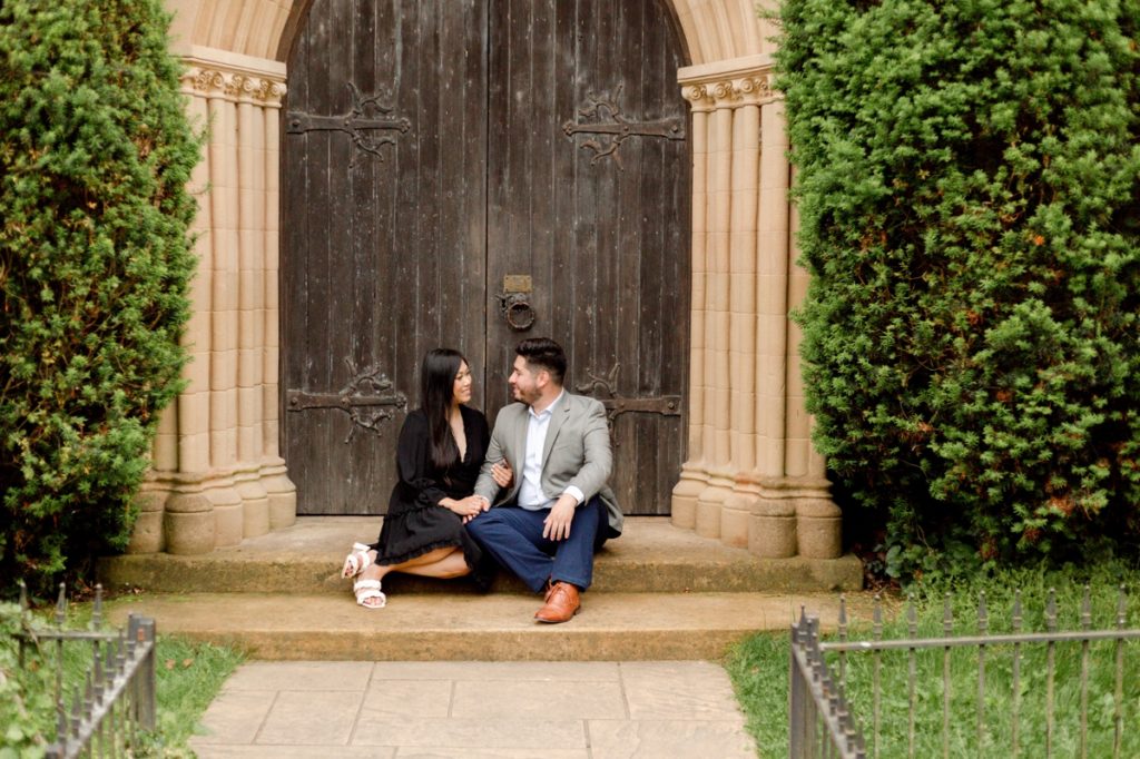 A man and his fiance sitting in front of a historic chapel during their portrait session at St. Catherine’s at Bell Gable.