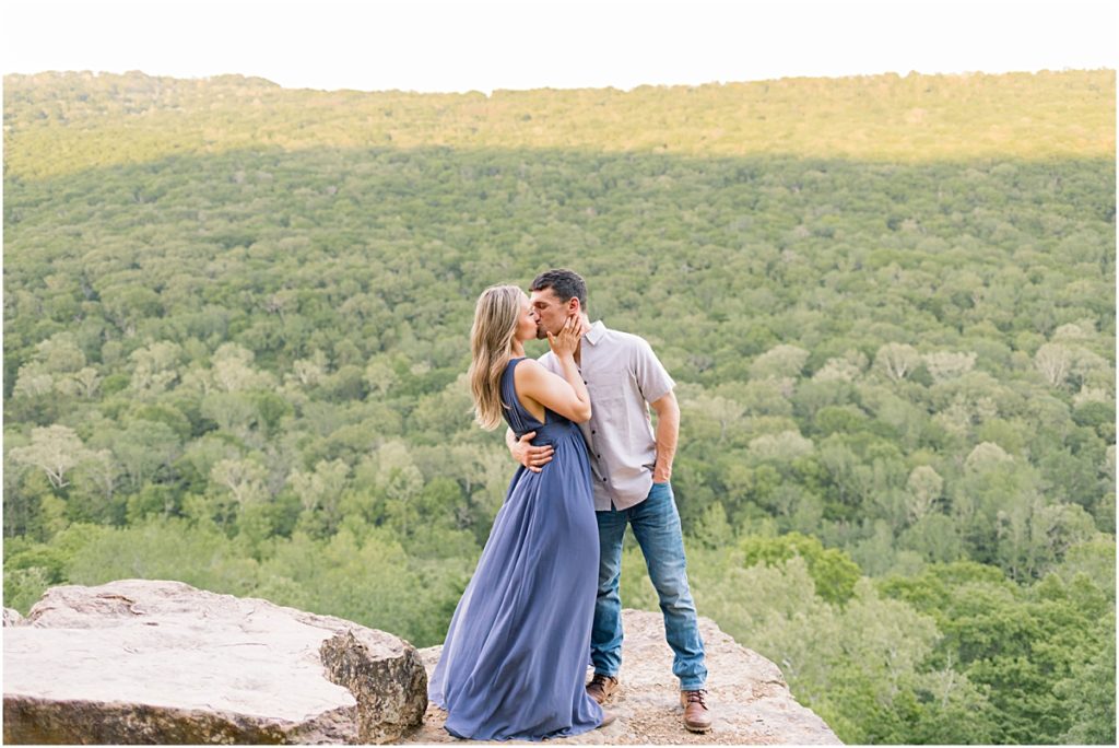 Sarah and Jarod dressed up and kissing on a cliff's edge in Devil's Den State Park.