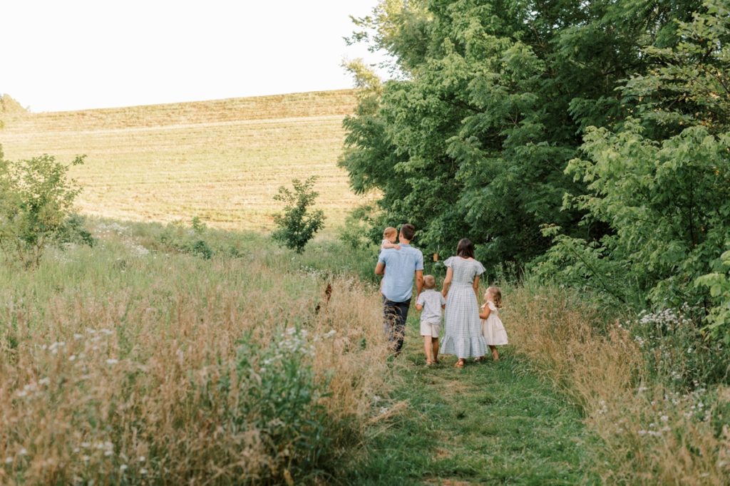 A family of five walking away towards a lush green field during their family session with Emily Quigley.