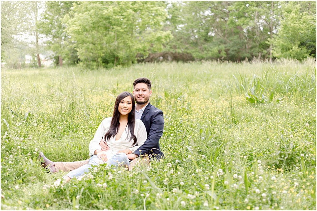 Couple sitting in open field with white wild flowers posing for a picture