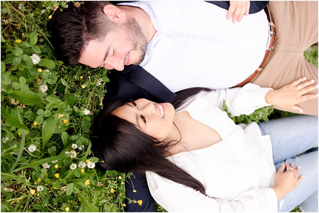 Jorge and Carina laying in a field among green brush and clover during Fayetteville Engagement Session