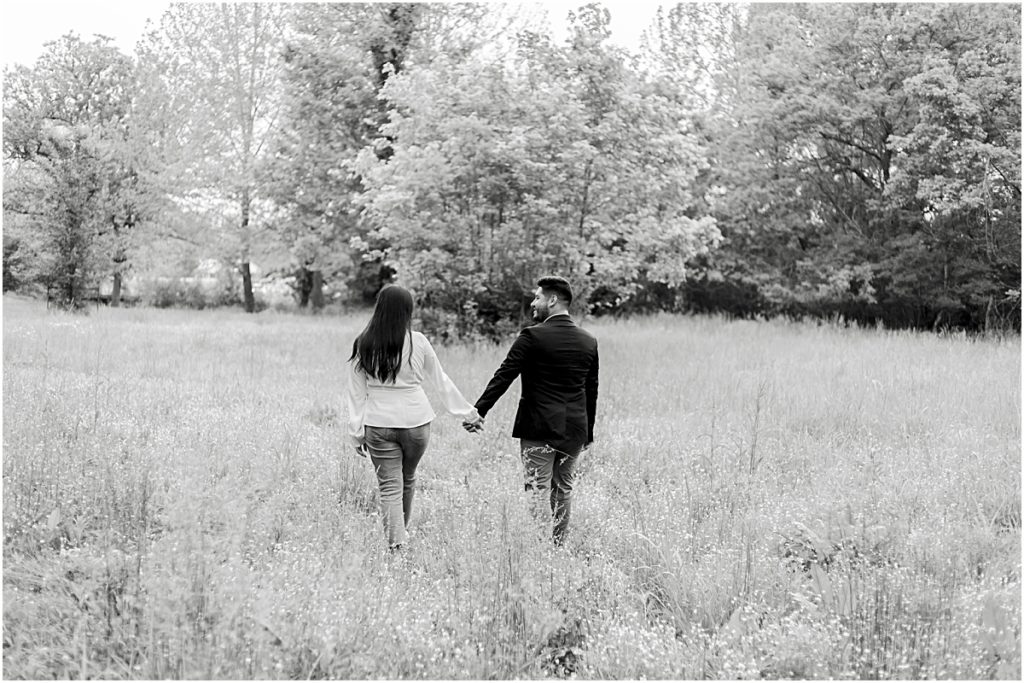 Jorge and Carina walking through a field, away from camera during a Fayetteville Engagement Session