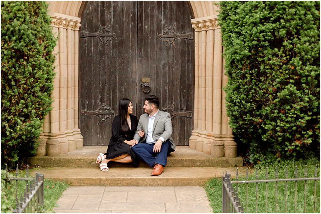 Jorge and Carina sitting in front of arched doors on the steps during Fayetteville Engagement Session