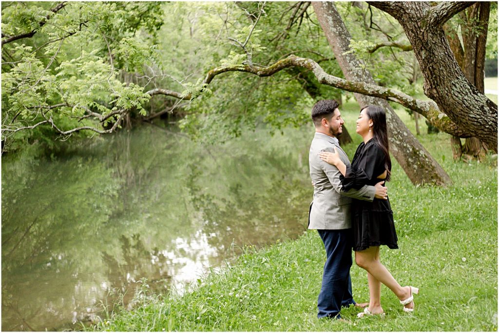 Jorge and Carina hugging beside a stream and underneath a tree during a Fayetteville Engagement Session