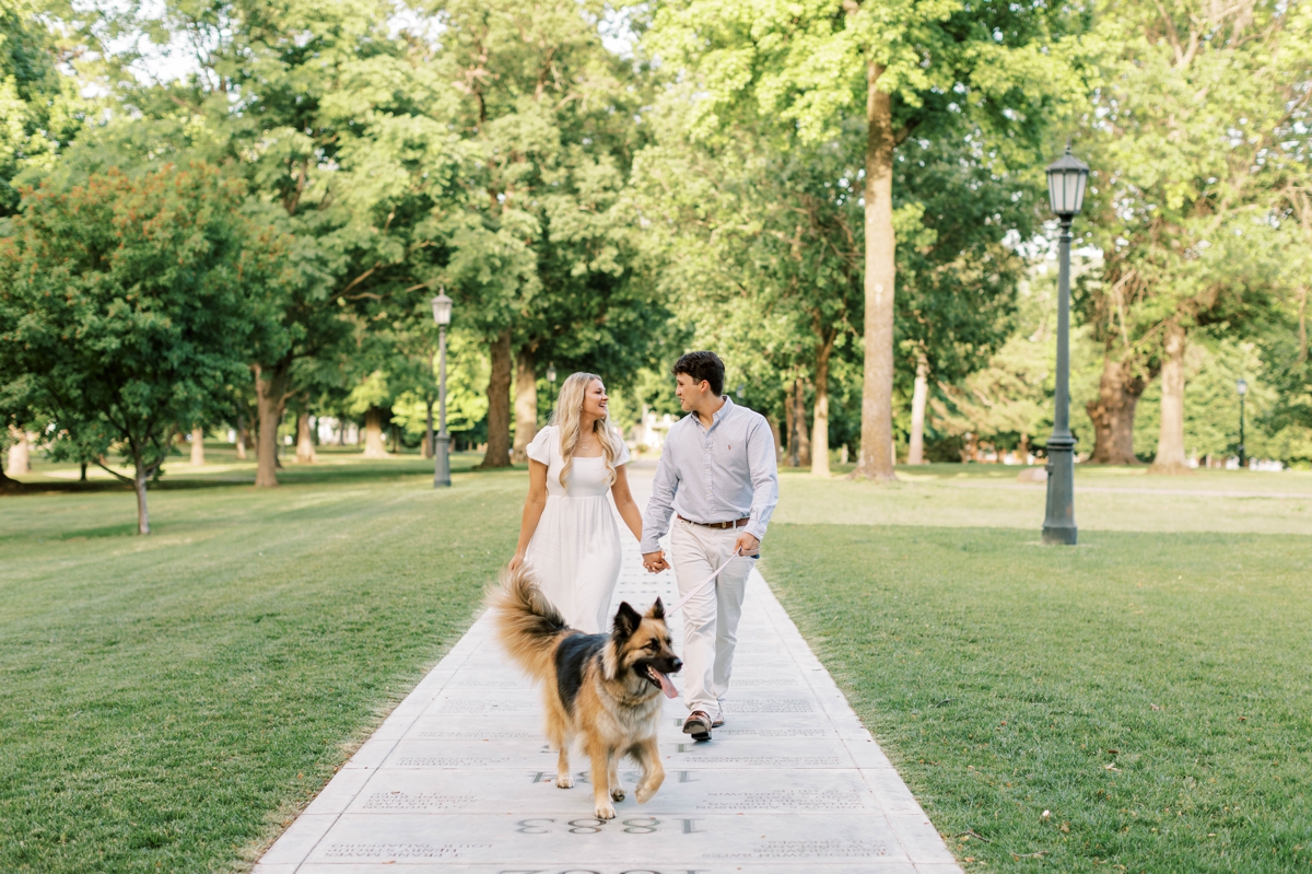 Couple walking along a sidewalk at the University of Arkansas with their dog.