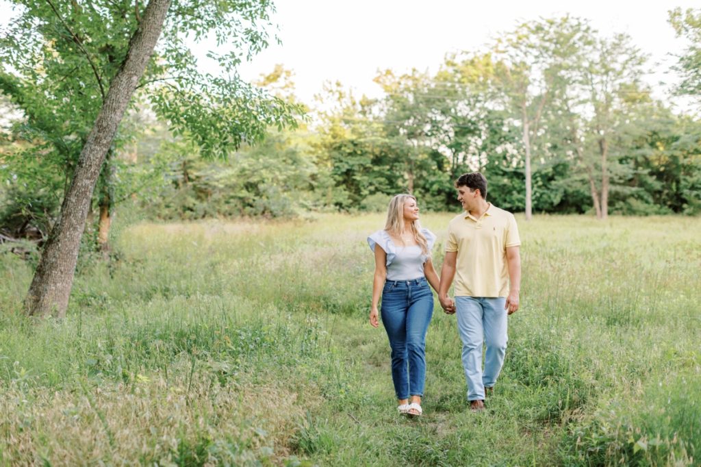 Couple walking through a field looking at each other during their engagement session in Arkansas.