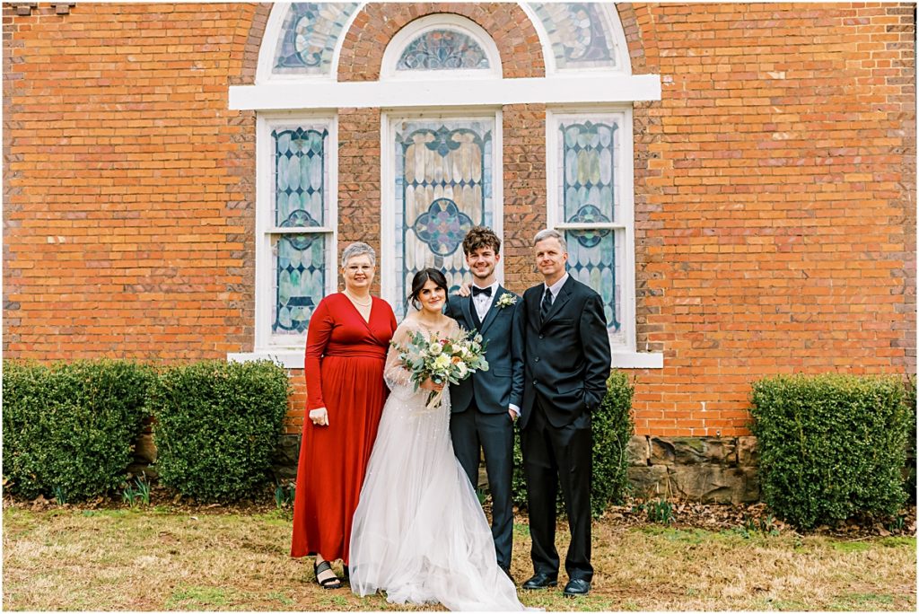 Emily and Lawrence outside church in front of stained glass windows, bushes and brick during Arkansas Elopement 