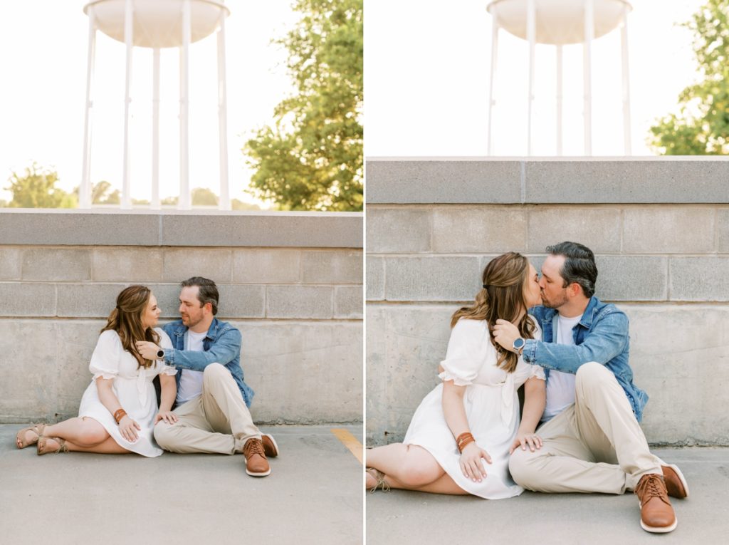 Couple sitting against a wall on top of a parking garage while they kiss each other during their engagement session
