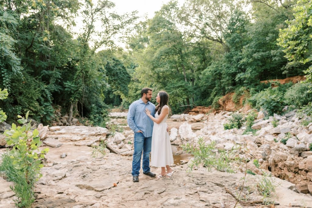 Couple standing on the rocky bed of a creek smiling at each other during their engagement session.