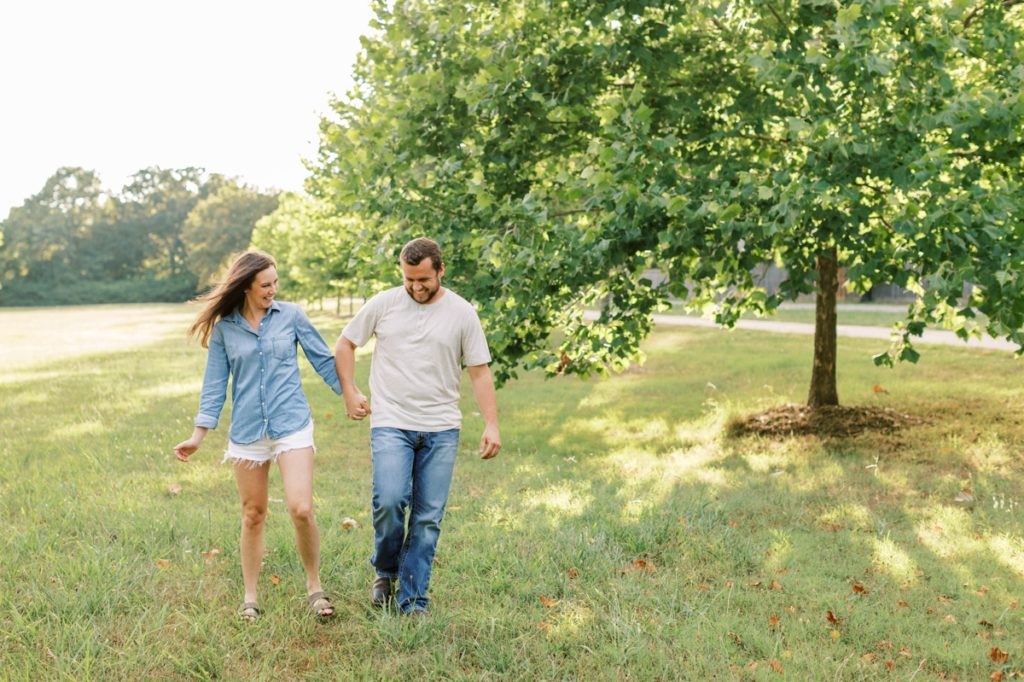 A couple walking through a field hip checking each other as they laugh during their engagement session