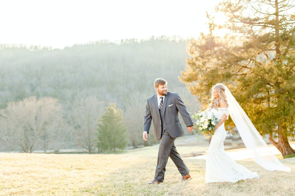 A couple walking across a grassy hill on their wedding day featuring a bouquet from Carey's Flowers.