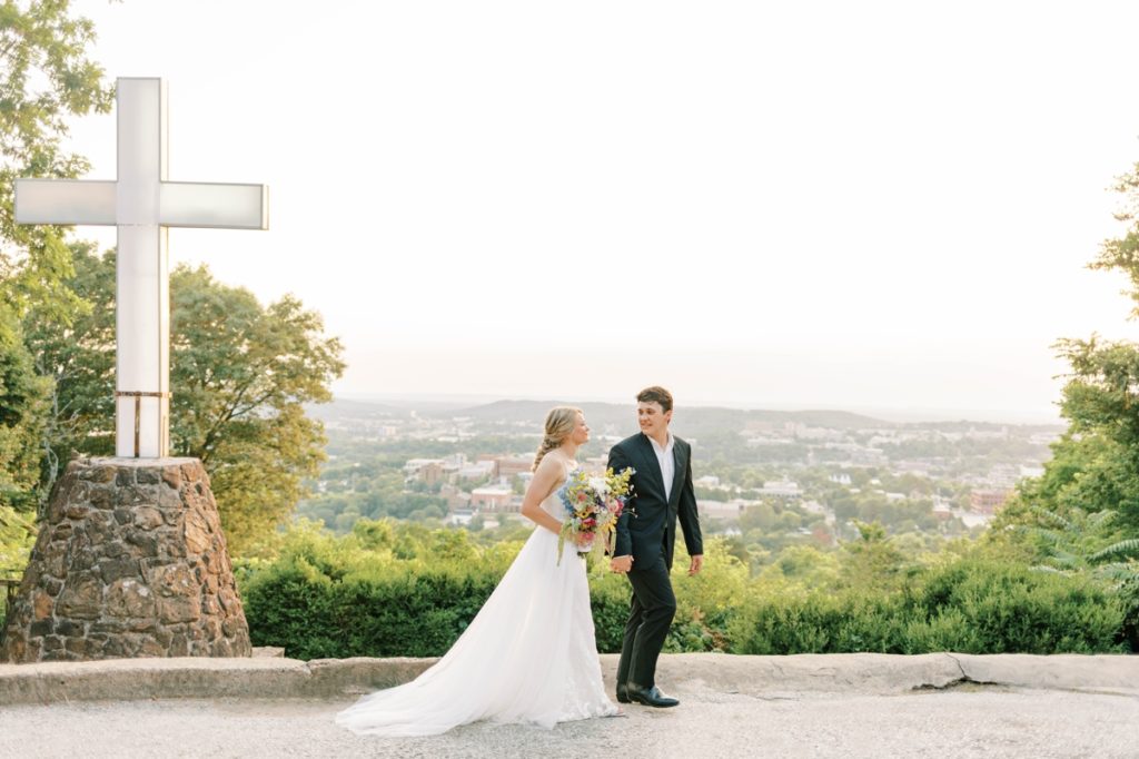 A bride and groom walking in front of a cross at Mt. Sequoyah on their wedding day.