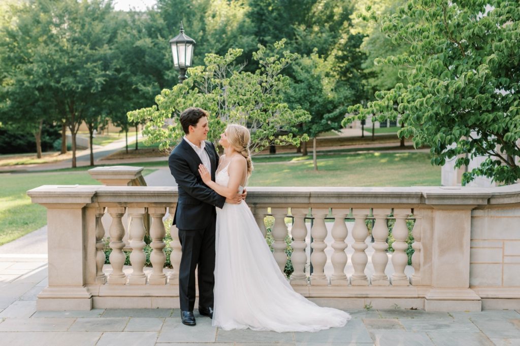 A bride and groom smiling at each other on a stone bridge at the University of Arkansas.