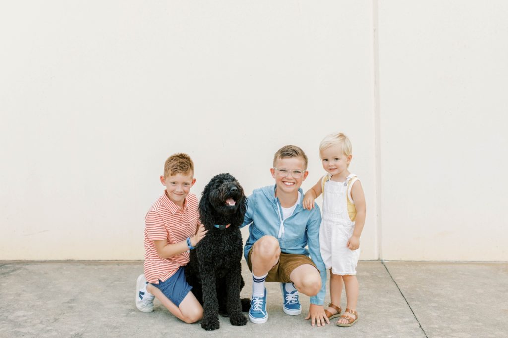 The three Flake boys kneeling down with their dog in front of a white while.