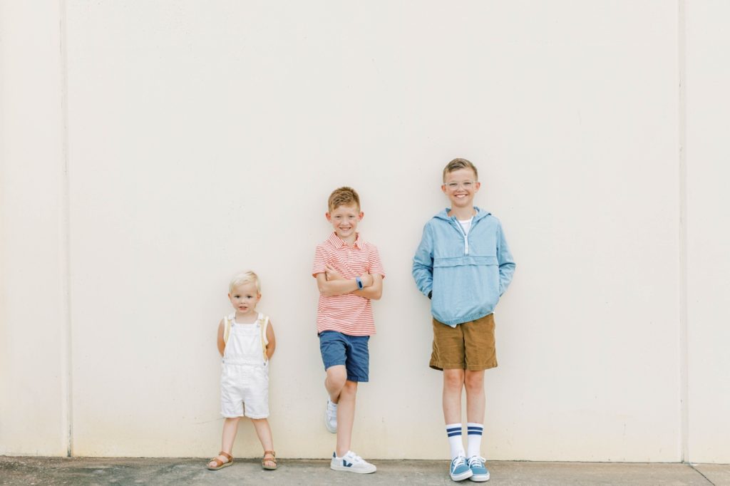 The three Flake kids leaning up against a white wall and smiling during their family session.