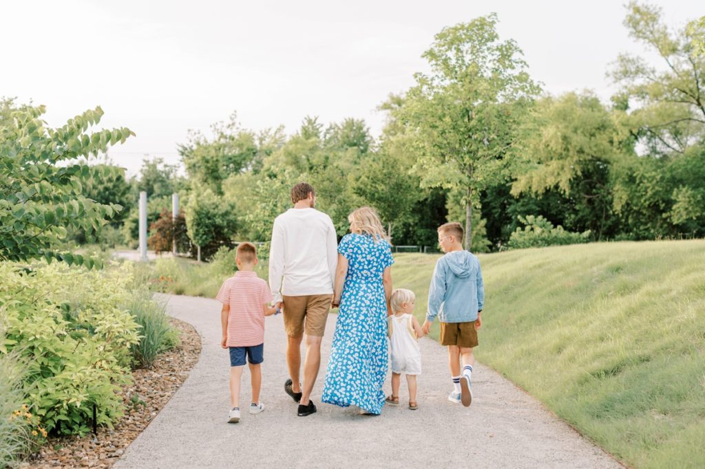 The Flake family holding hands and walking away from the camera down a path in a park.