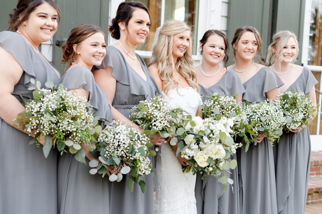 A bride and her bridesmaids smiling off into the distance while they hold their wedding day bouquets.