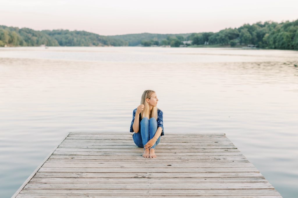 Natalie sitting on a dock in front of a lake playing with her hair during her senior session with Emily Quigley Photography.