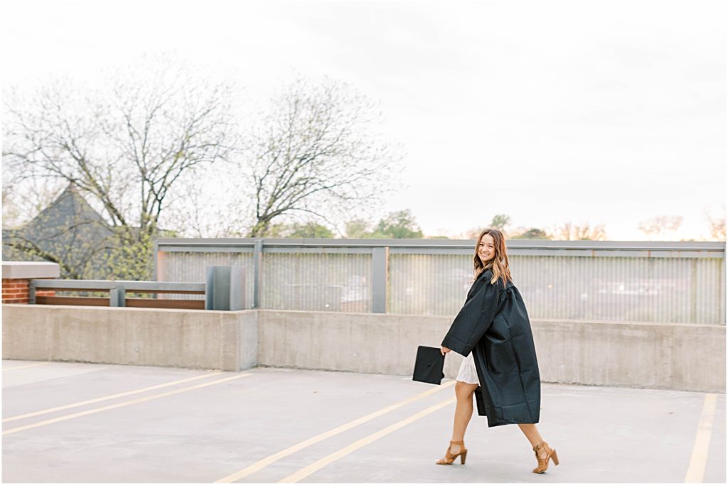 Kaiyah walking across the top of a parking garage wearing her graduation gown and holding her cap in her hand.