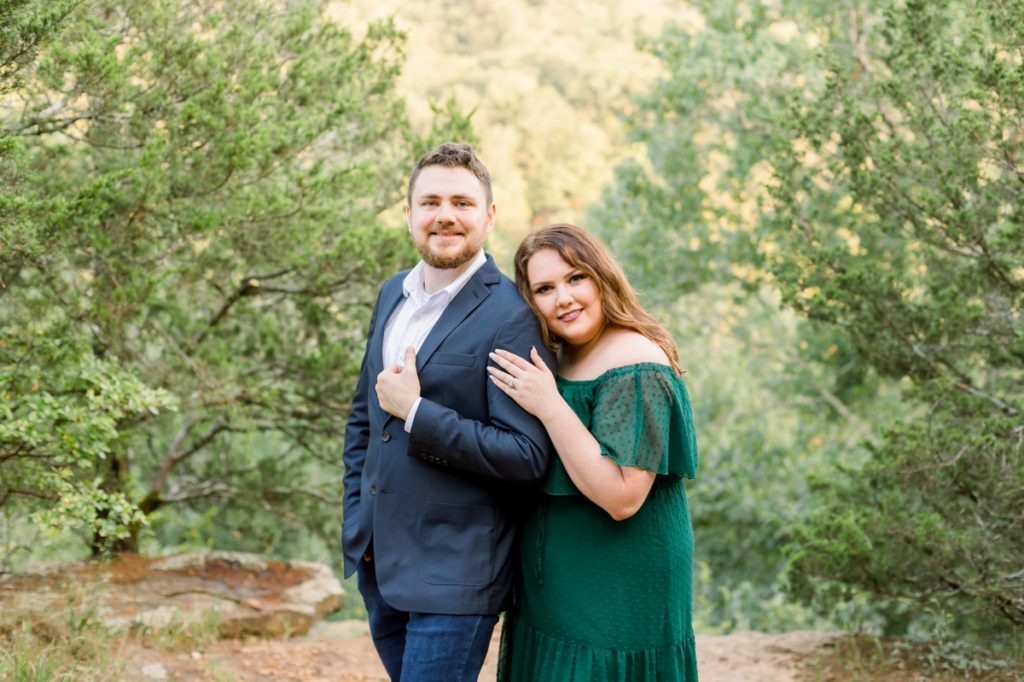 A woman in a green dress leaning on her fiance's shoulder during their engagement session.